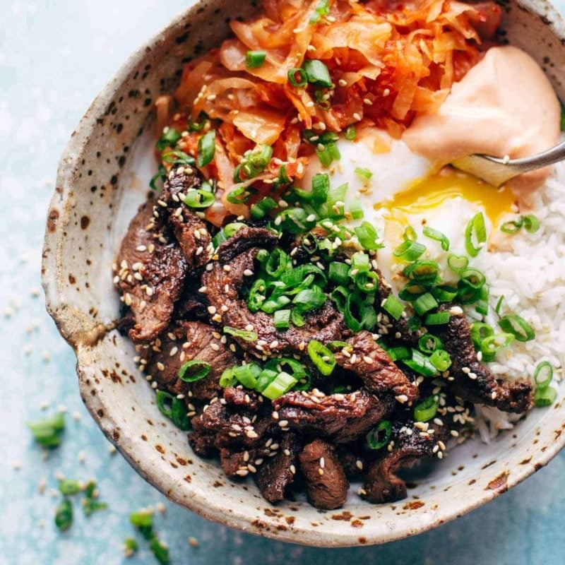 Korean beef along with carrot, onion and spicy mayo in a bowl with a spoon.