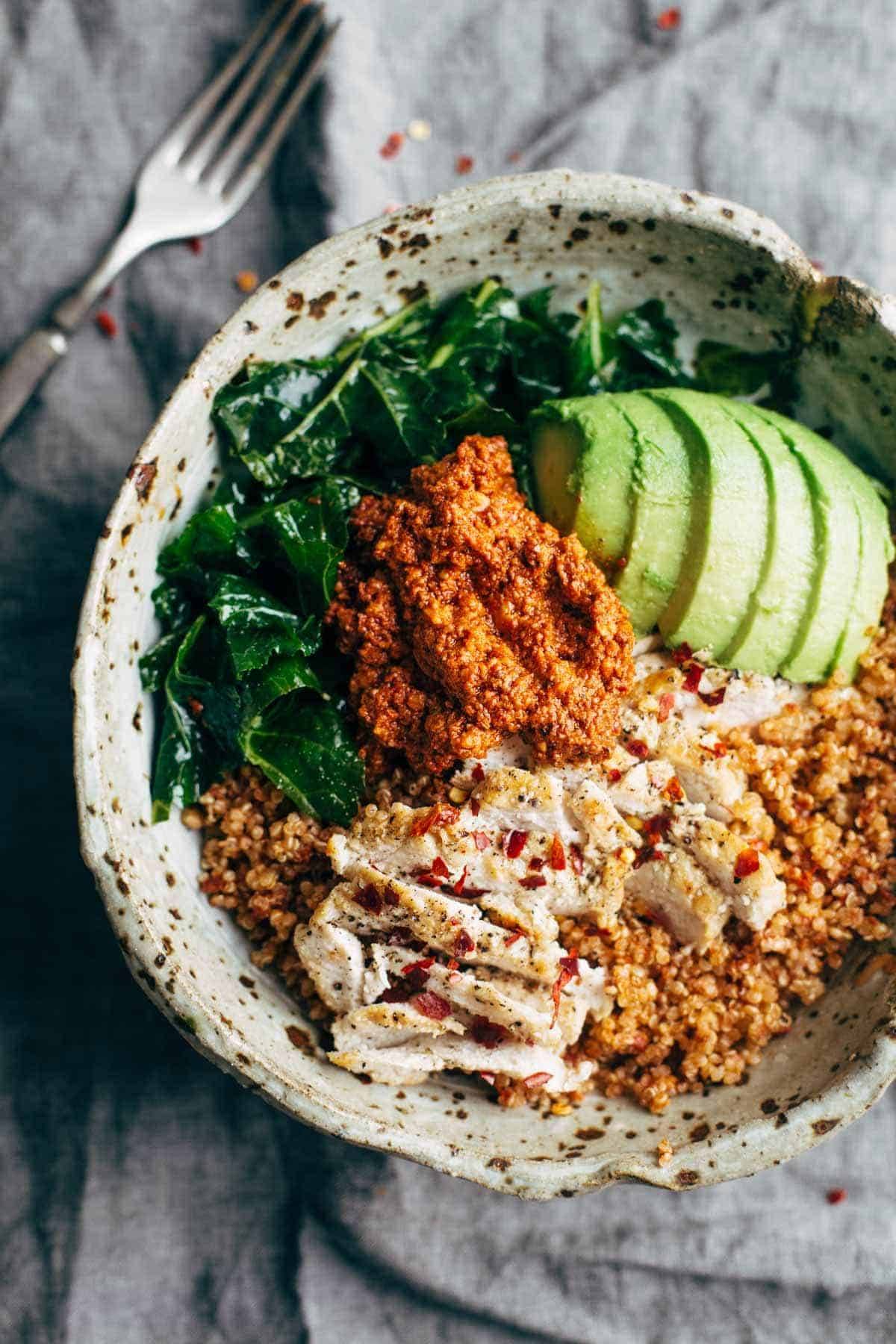 kale and chicken quinoa bowl with sun dried tomato sauce with a fork