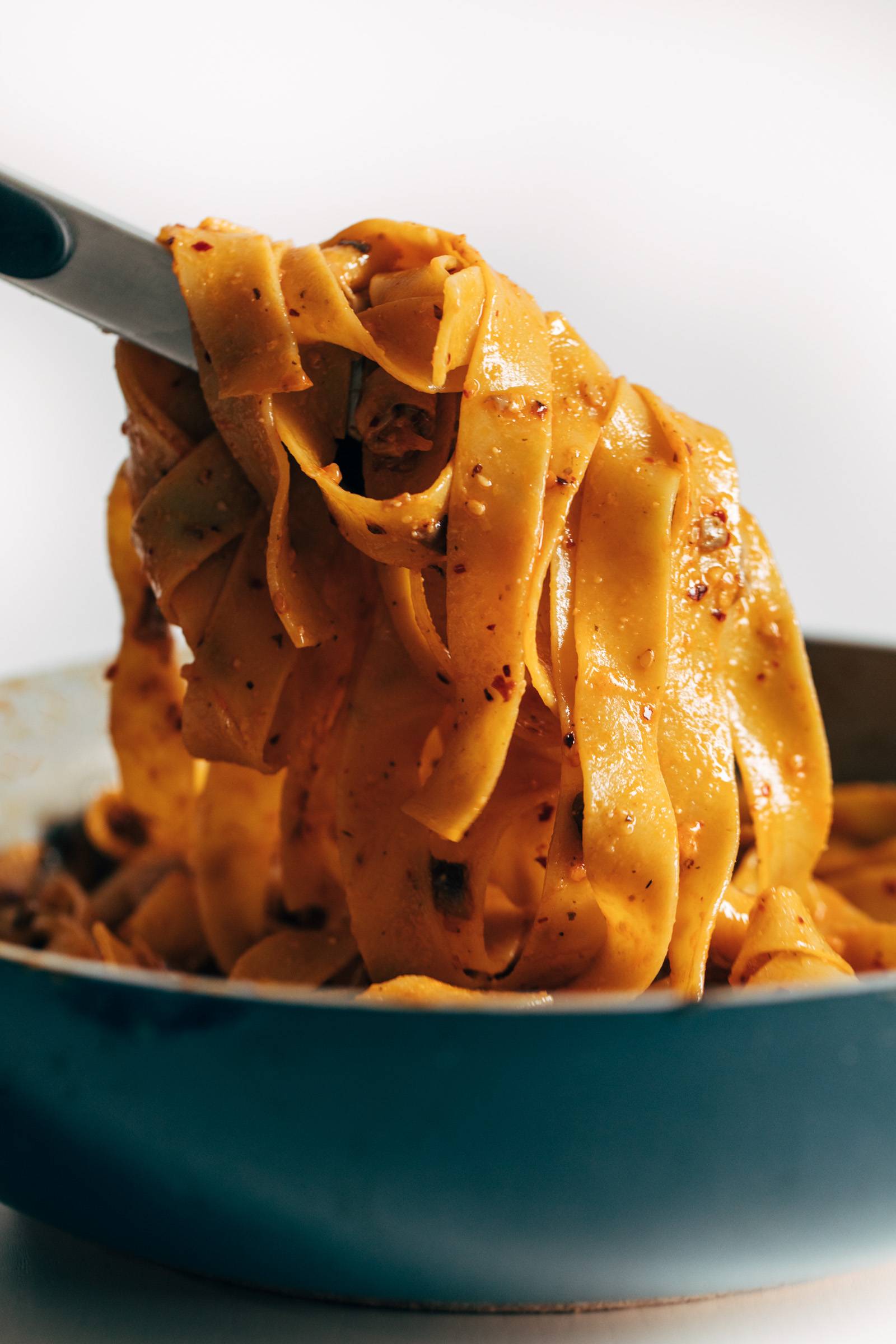 Tongs pulling up pappardelle noodles