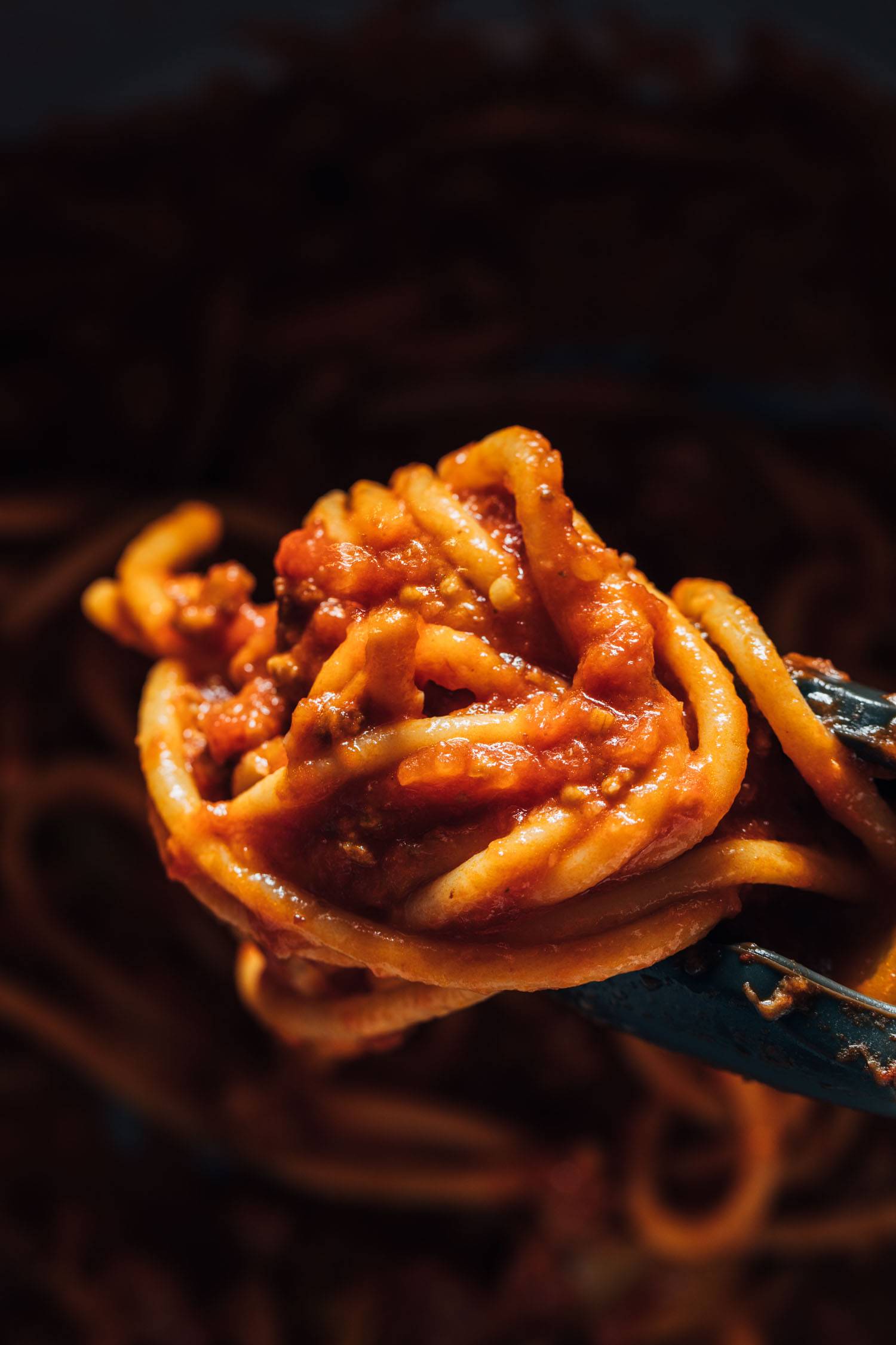 Tongs holding bucatini with red sauce.