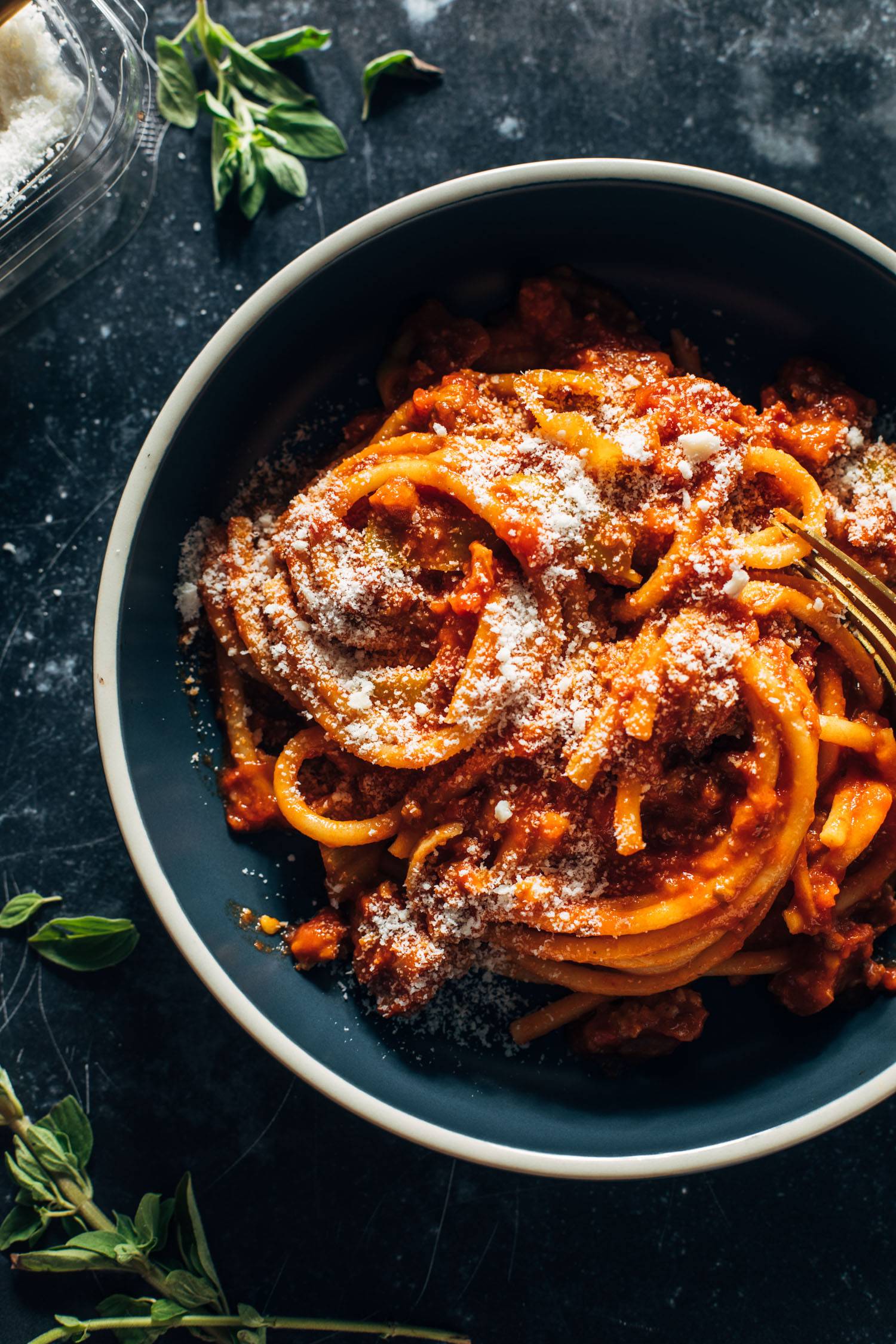 Bucatini in a bowl with pecorino sprinkled on top.