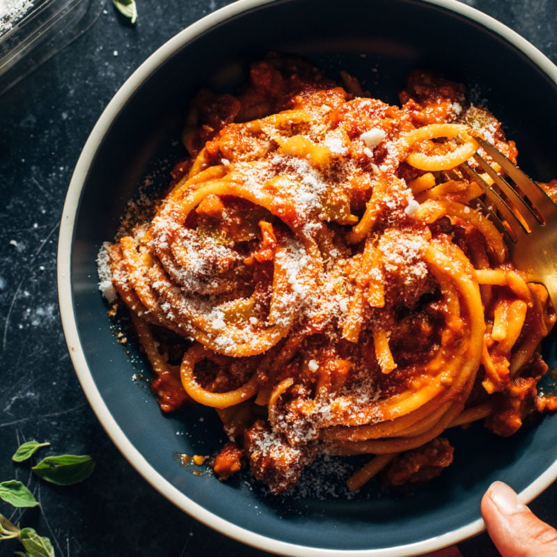 Bucatini in a bowl with red sauce and pecorino on top.