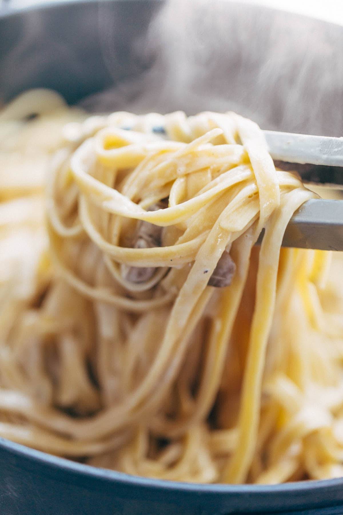 Mushroom Fettuccine in pan bring served with tongs.