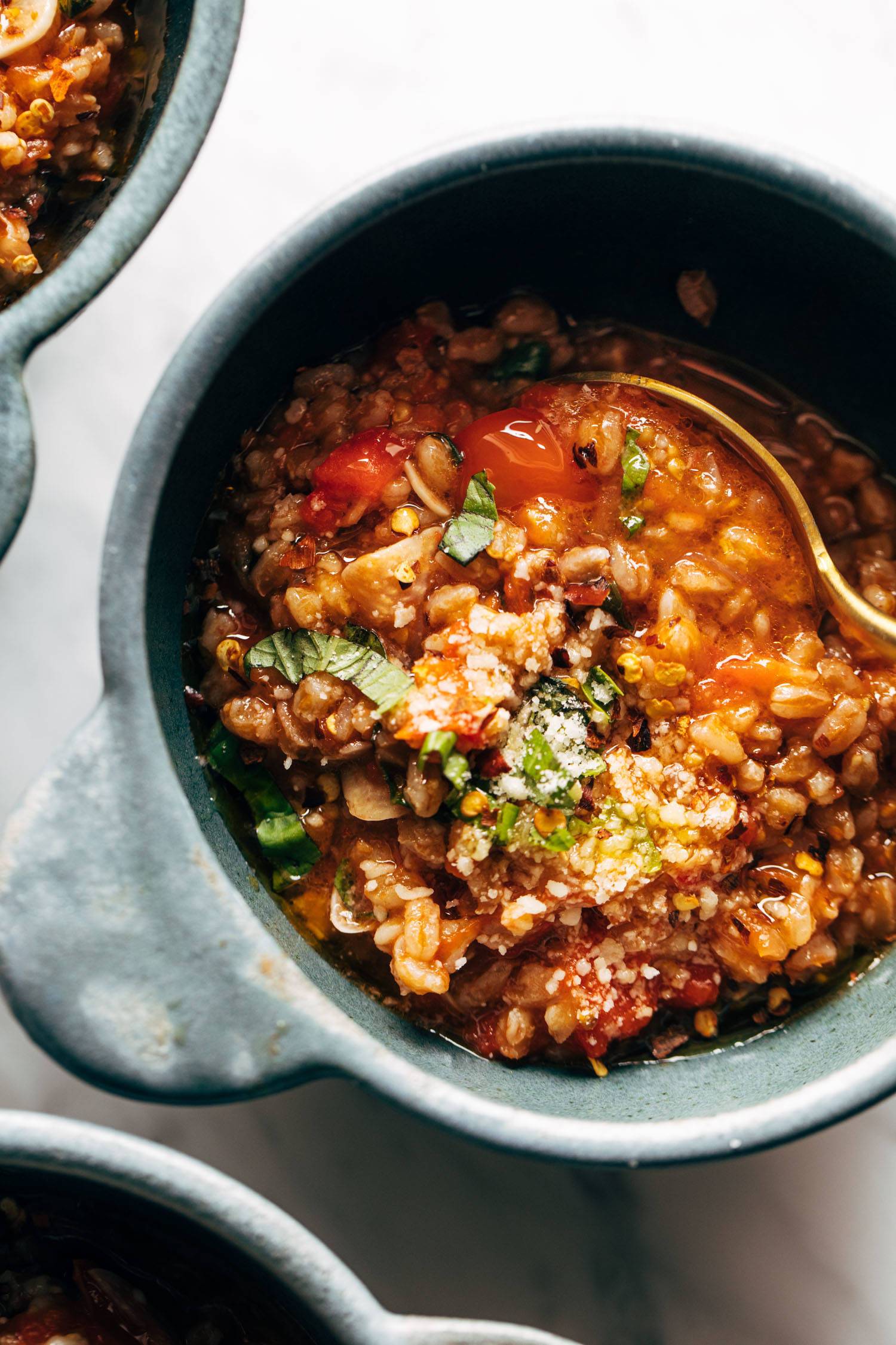 Farro, tomatoes, and kale in blue bowls with a gold spoon. There are fresh herbs and Parmesan cheese sprinkled on top. 