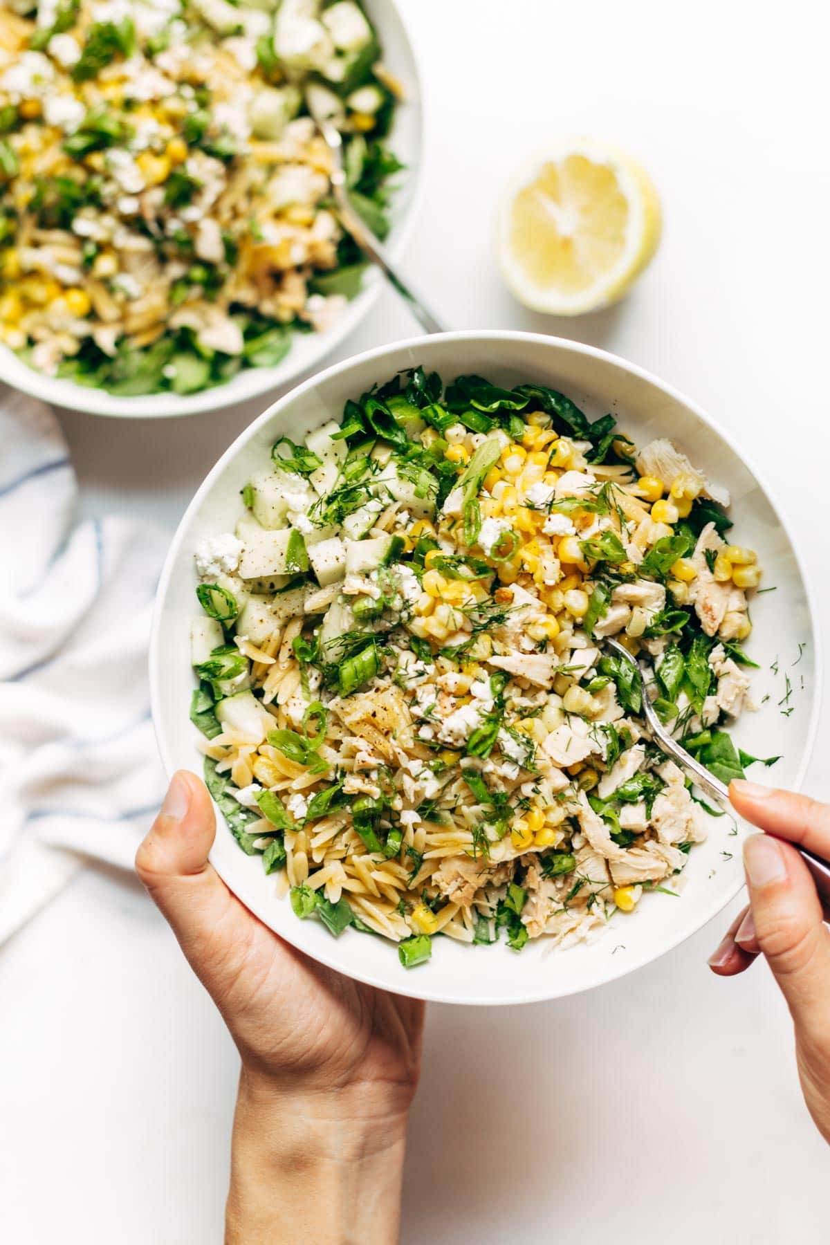 Hands holding Orzo Summer Salad with a fork.