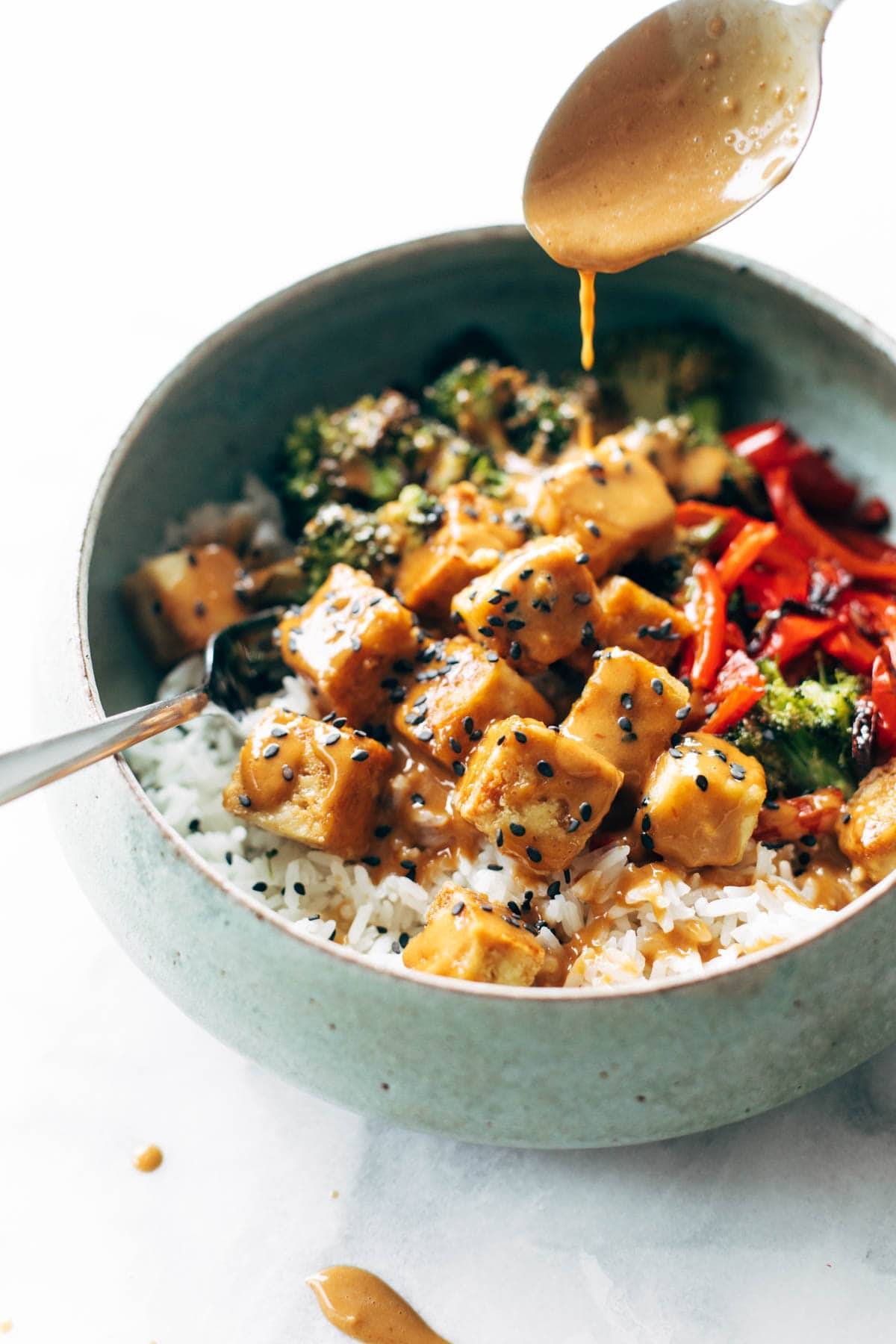 Drizzling peanut sauce on peanut tofu bowl.