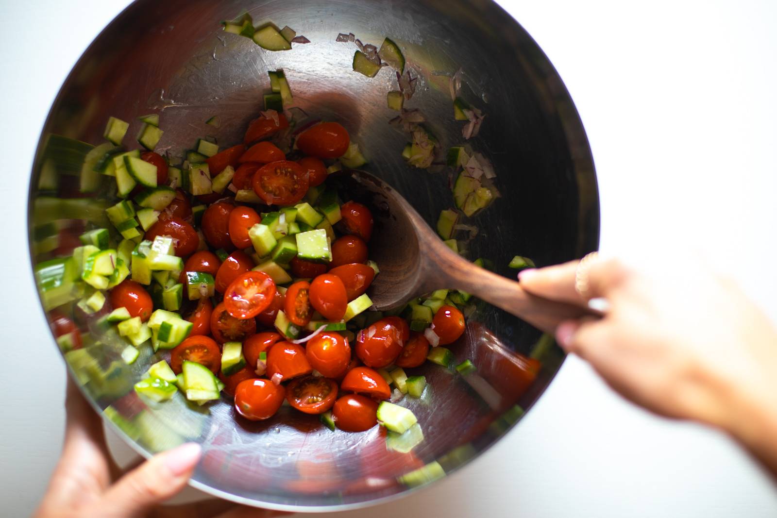 Cucumber and tomato salad being tossed in a bowl.