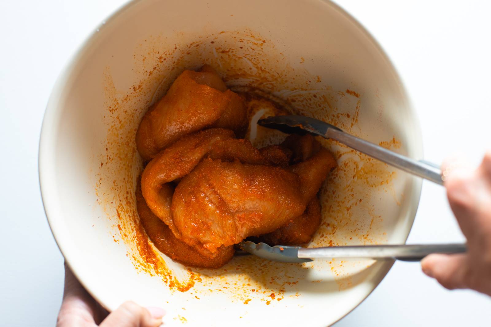 Raw chicken being tossed with spices in a bowl.