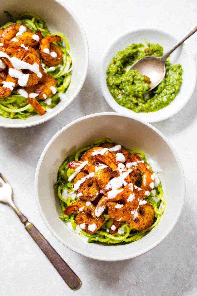 Zucchini noodles in a bowl with pesto and shrimp on top.