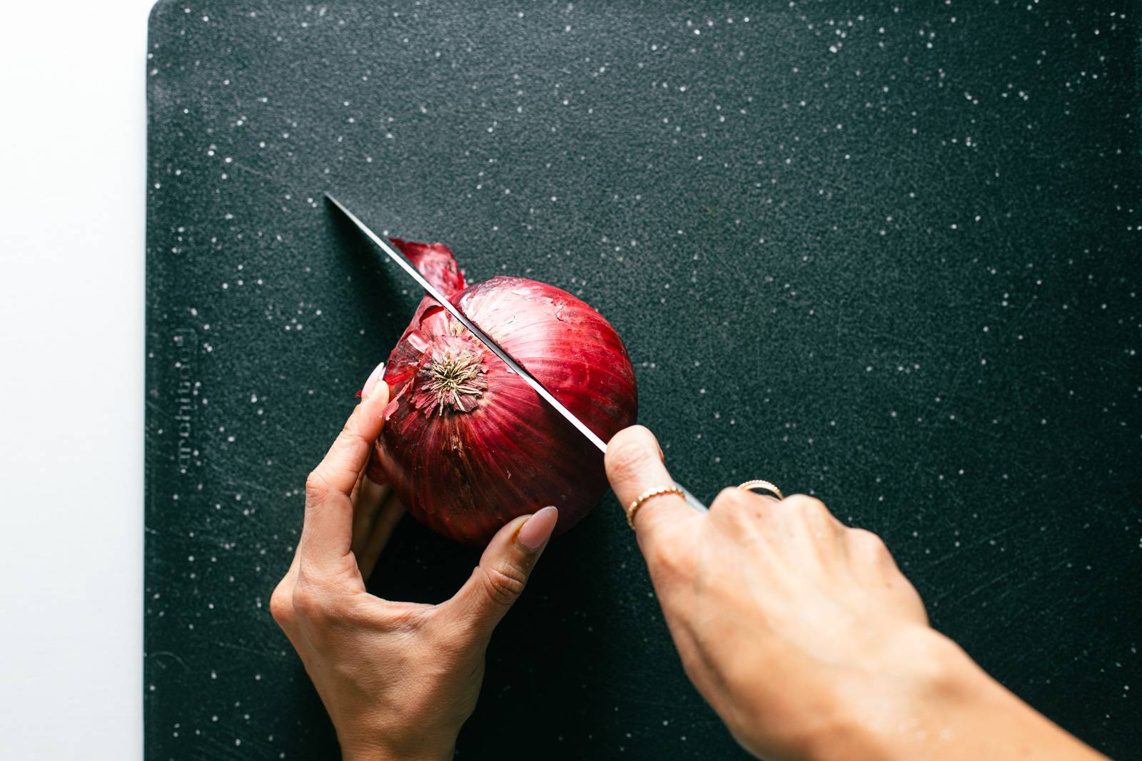 White hand cutting red onion in half