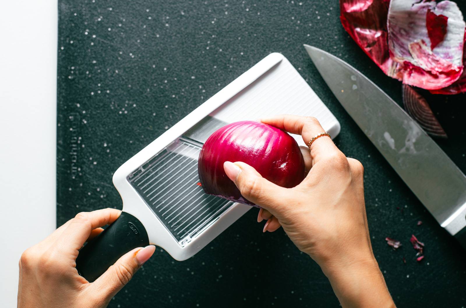 White hand cutting red onion on white mandoline.