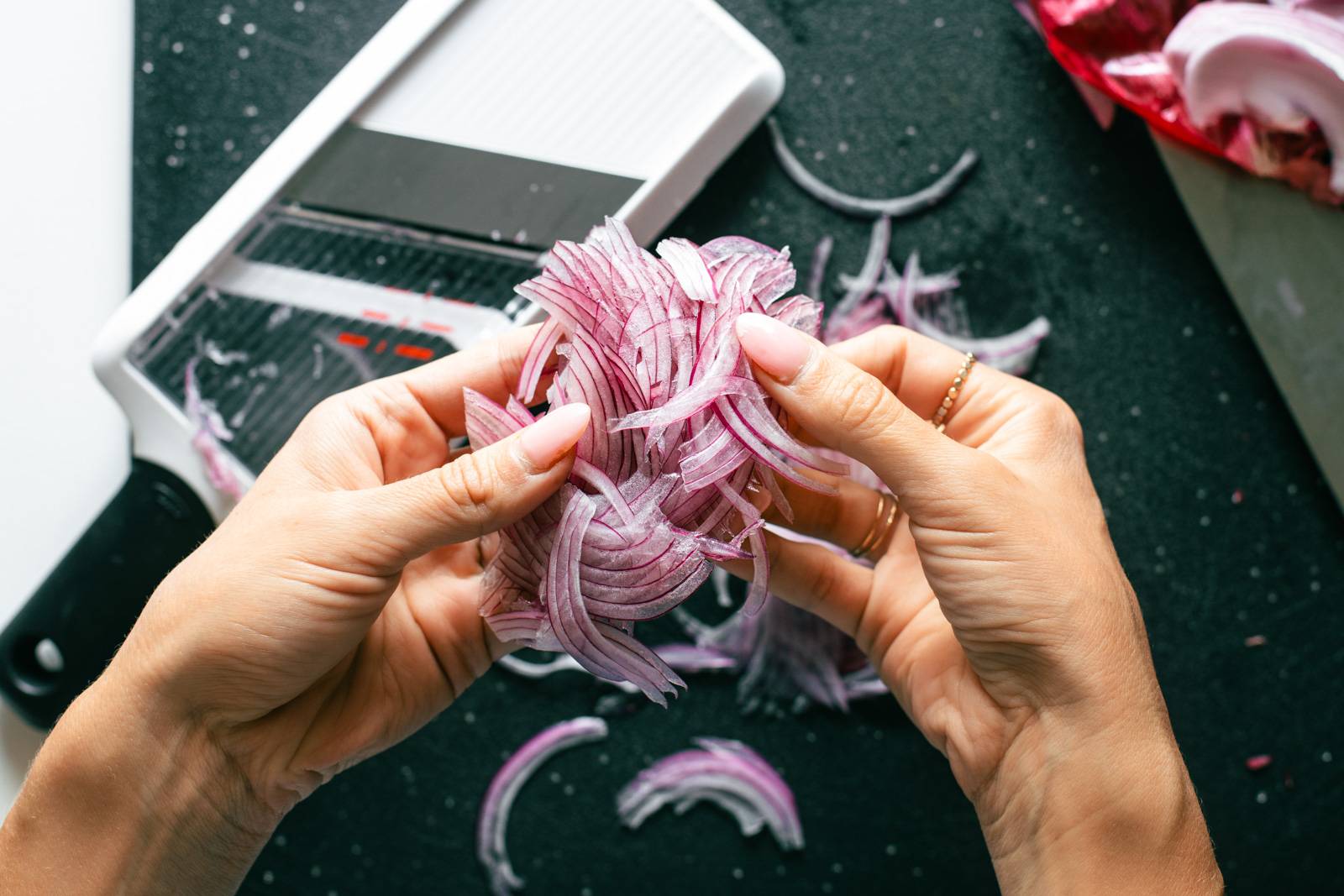 White hand holding thinly sliced red onions.