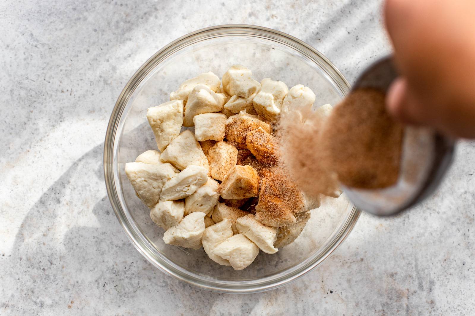 Dough pieces being tossed with cinnamon sugar.