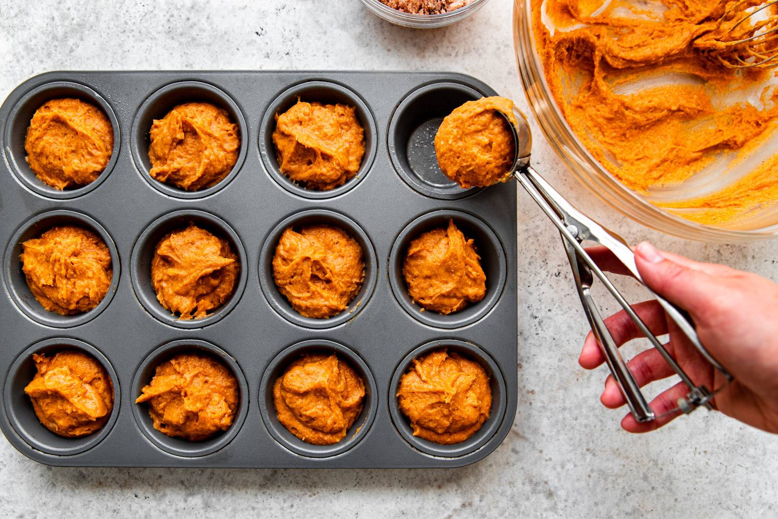 Scooping pumpkin muffin batter into a muffin tin.