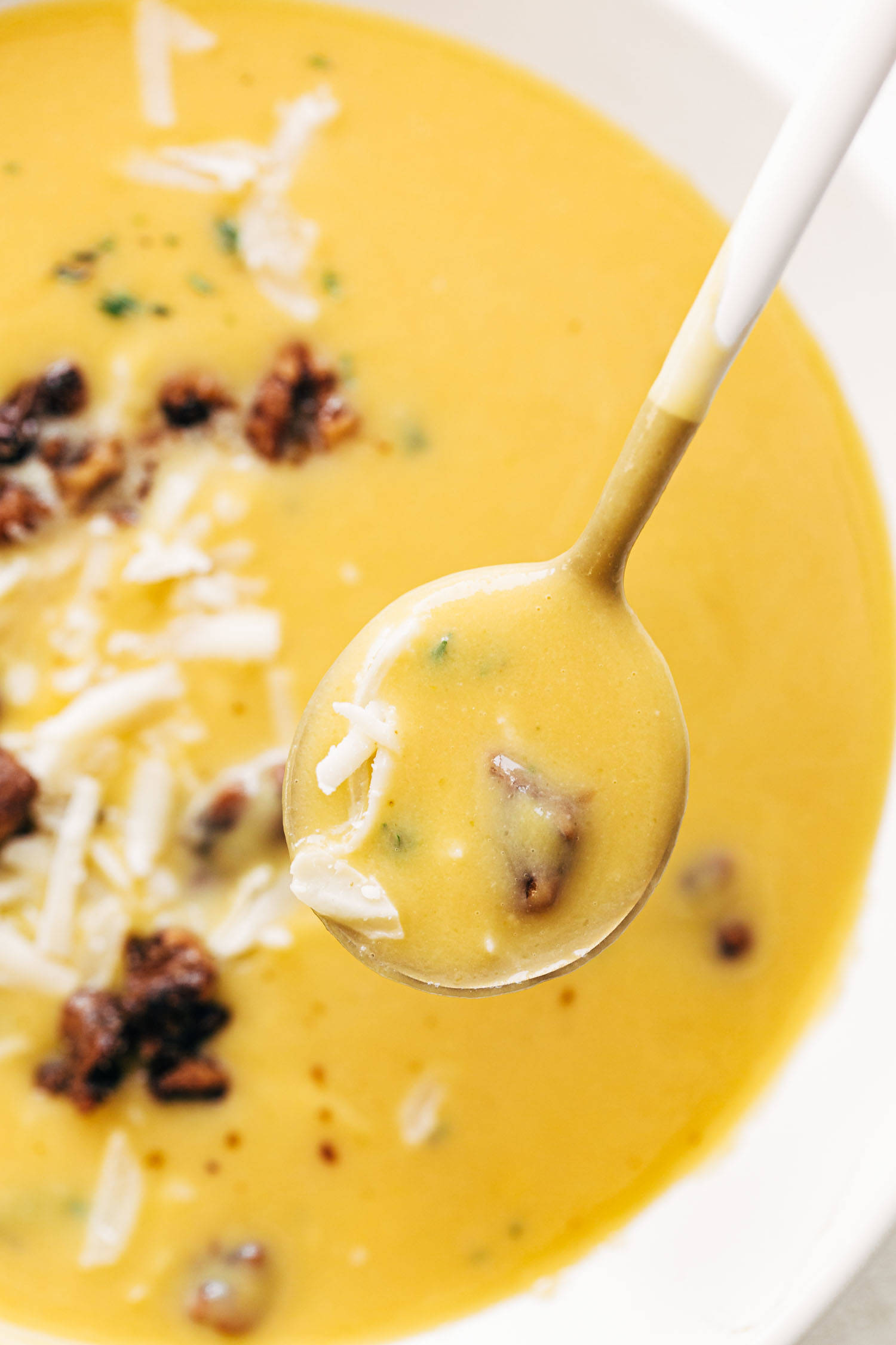 Spoon scooping up pumpkin soup with walnut crispies.