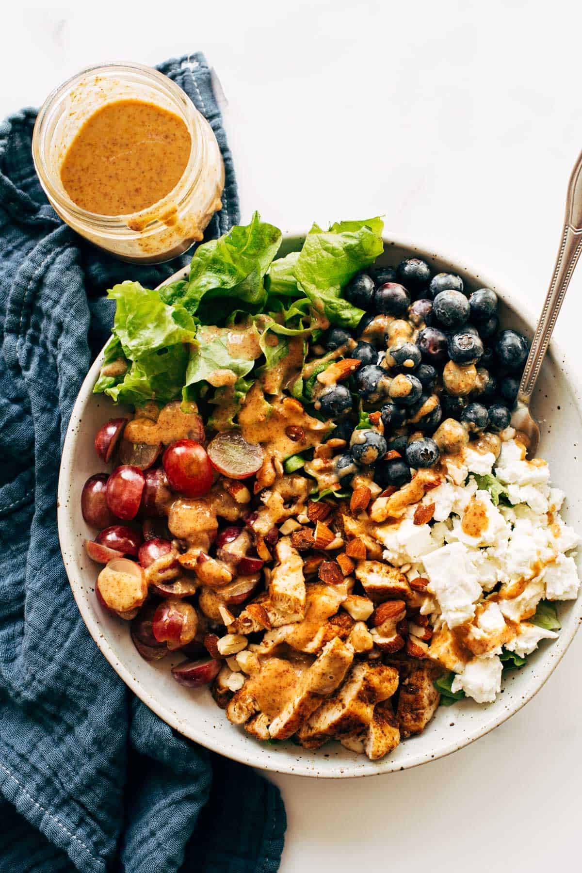 Rainbow chicken salad in a bowl with a fork with almond honey mustard dressing on the side