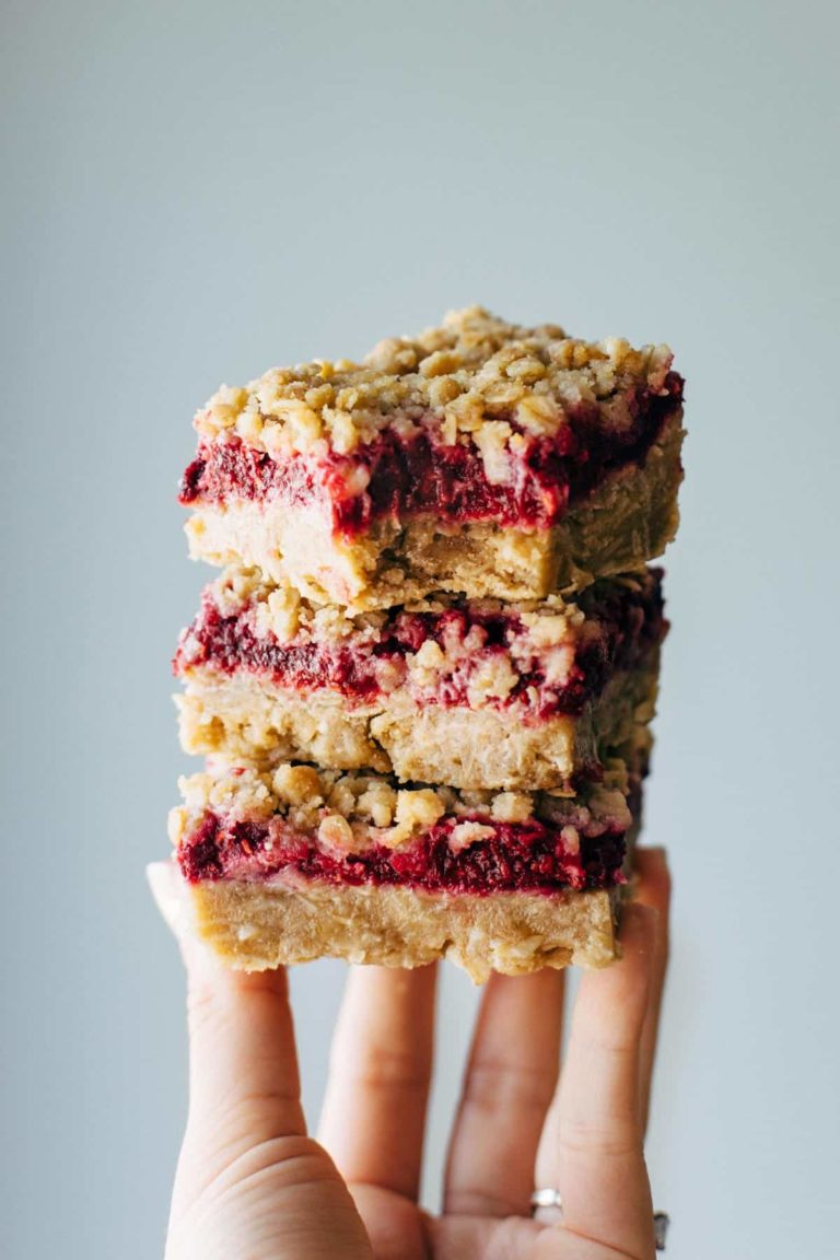 Raspberry crumble bars stacked with a hand.