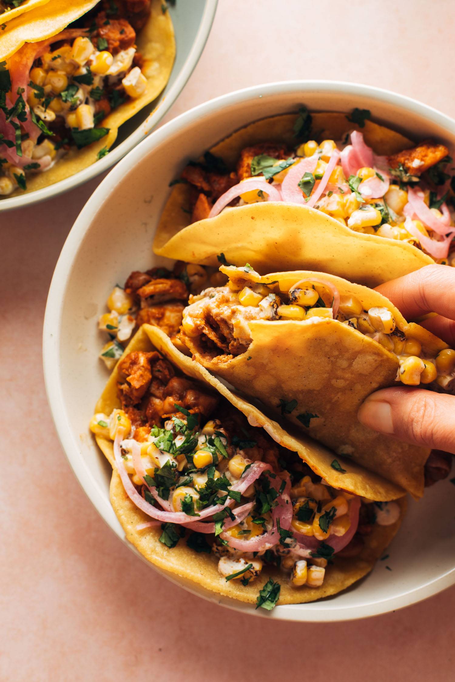 White hand holding chicken tacos on a plate