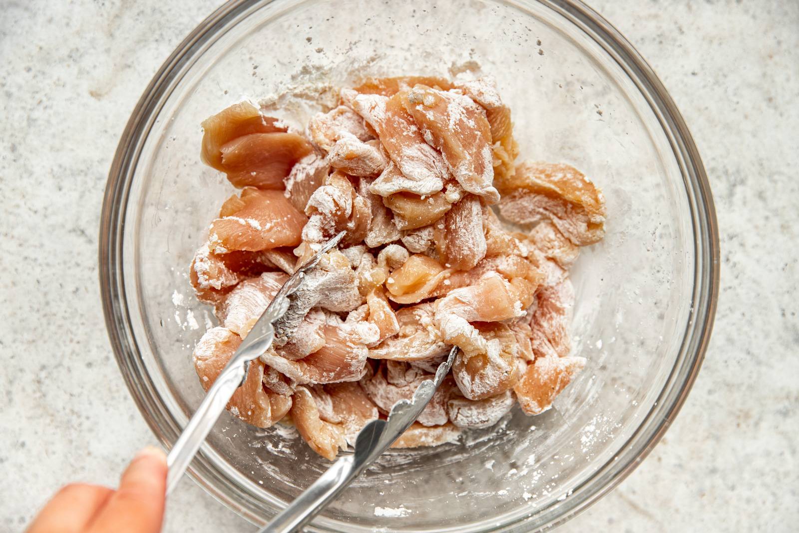 Cornstarch gets added to cut up raw chicken pieces in a bowl