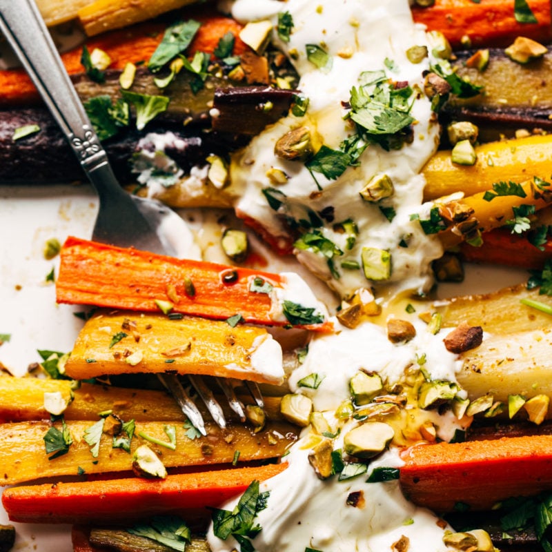 Heirloom carrots on a sheet pan with yogurt sauce and a fork.