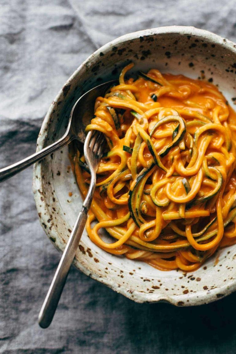 Zucchini noodles in a bowl with creamy red pepper sauce.