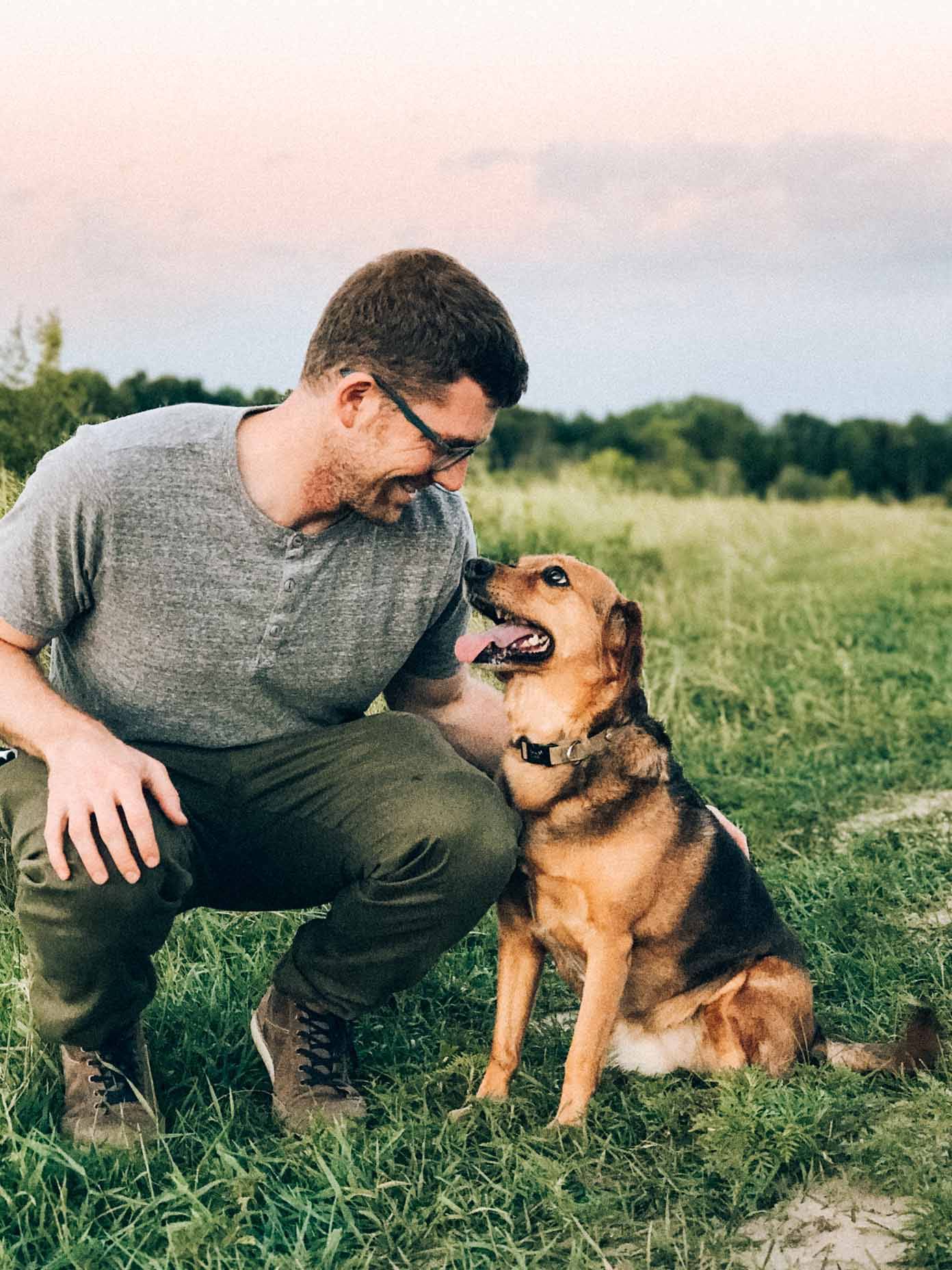 Man kneeling with a dog in an open field.