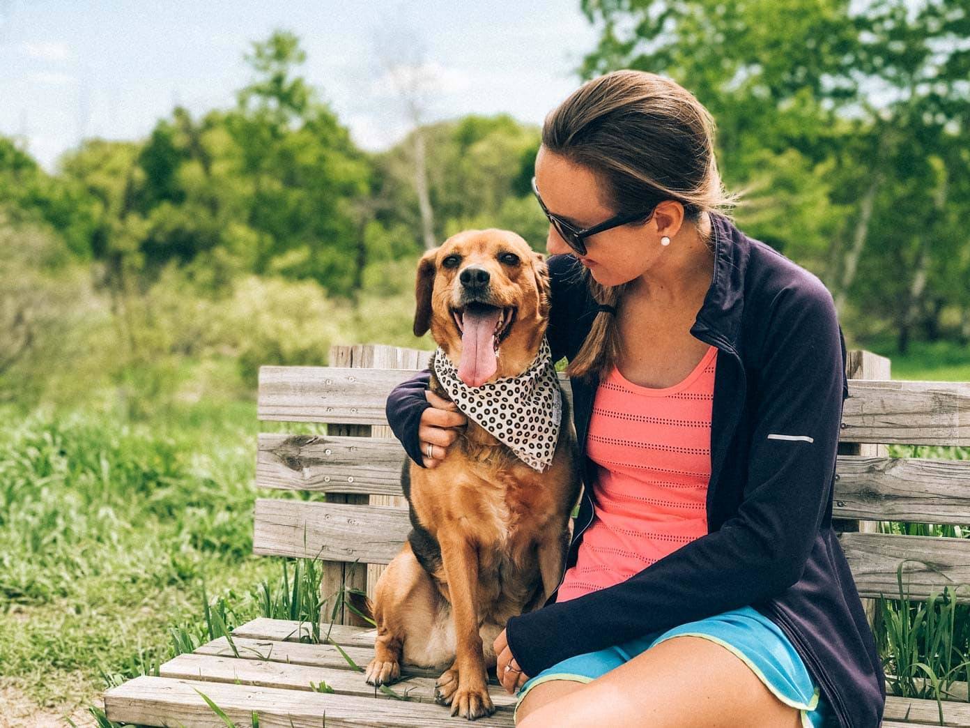 Woman sitting on a park bench with a dog in a bandana.