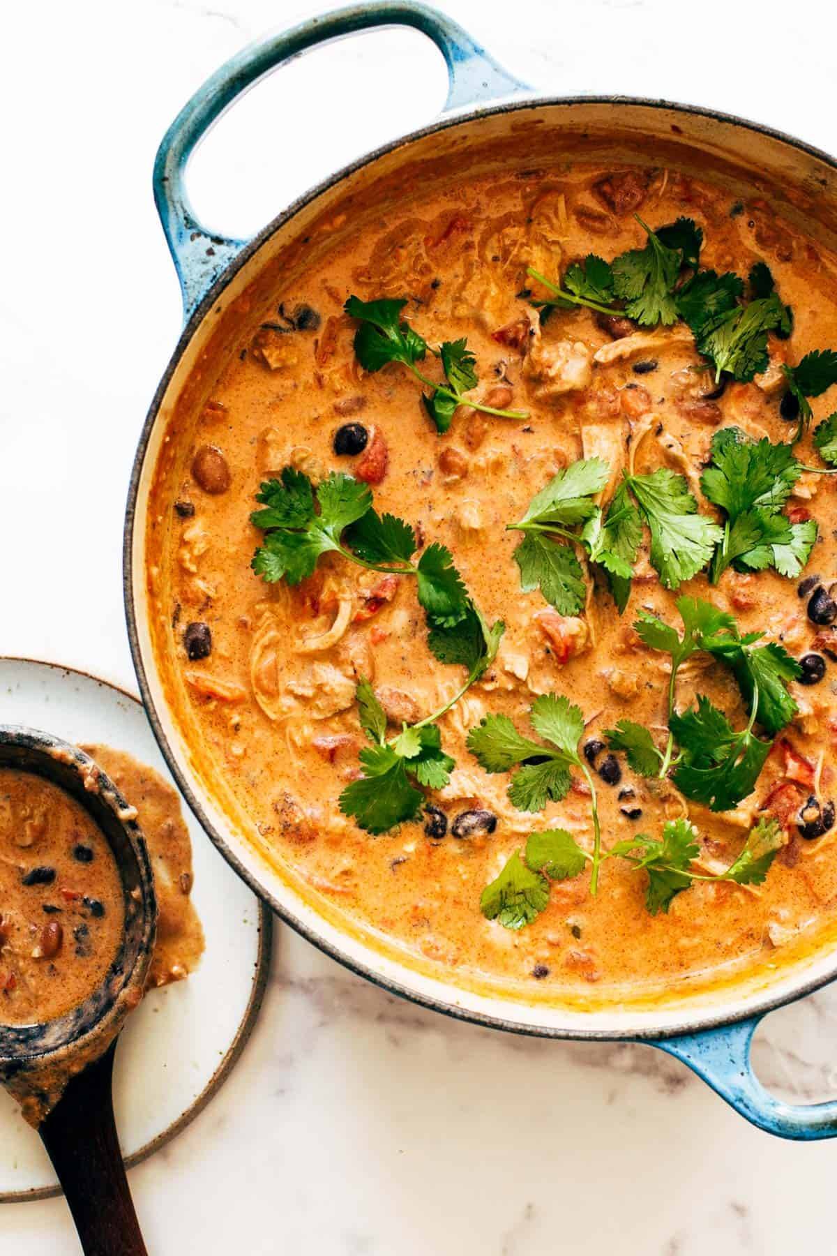 A pot full of white chicken chili with green garnishments.