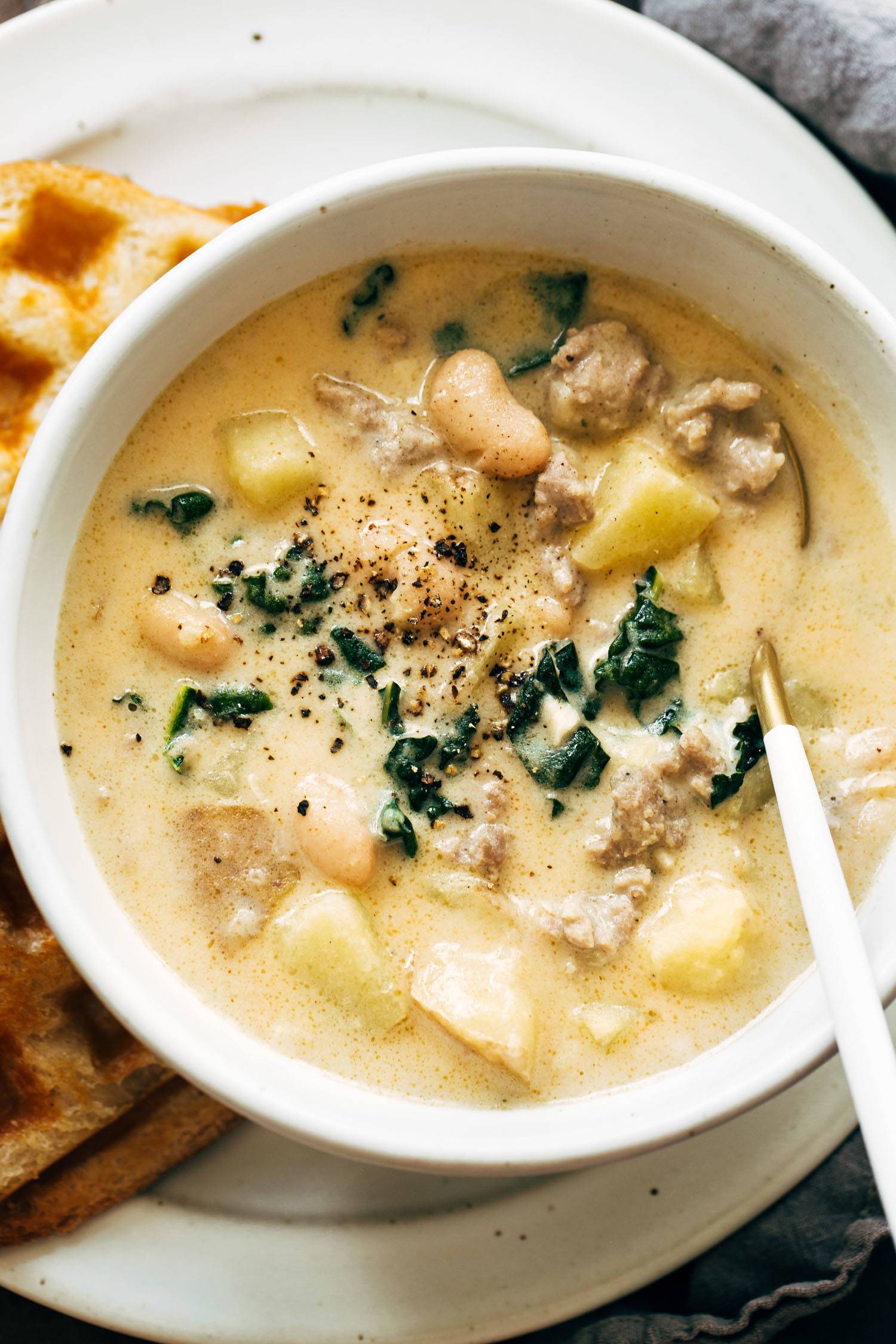 Sausage, bean, and kale soup in a bowl with a spoon. 