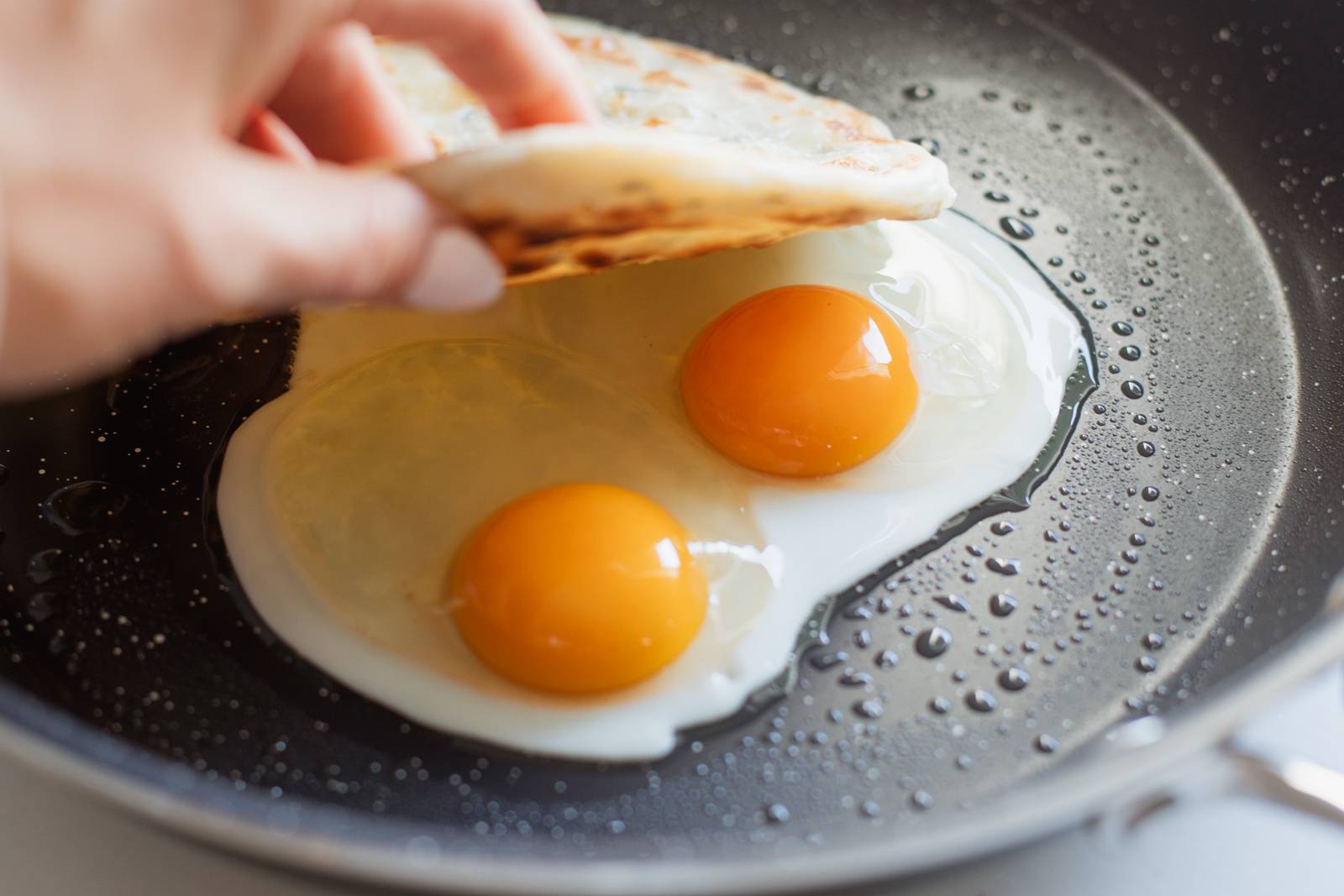 Eggs in a pan, placing scallion pancake on top.