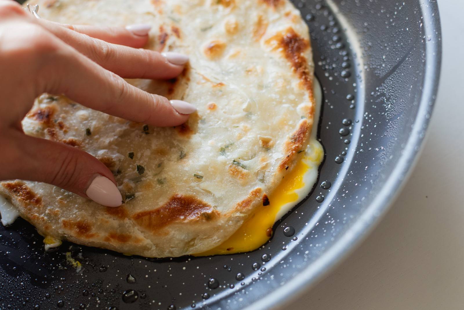 Placing scallion pancake on top of eggs in a pan.