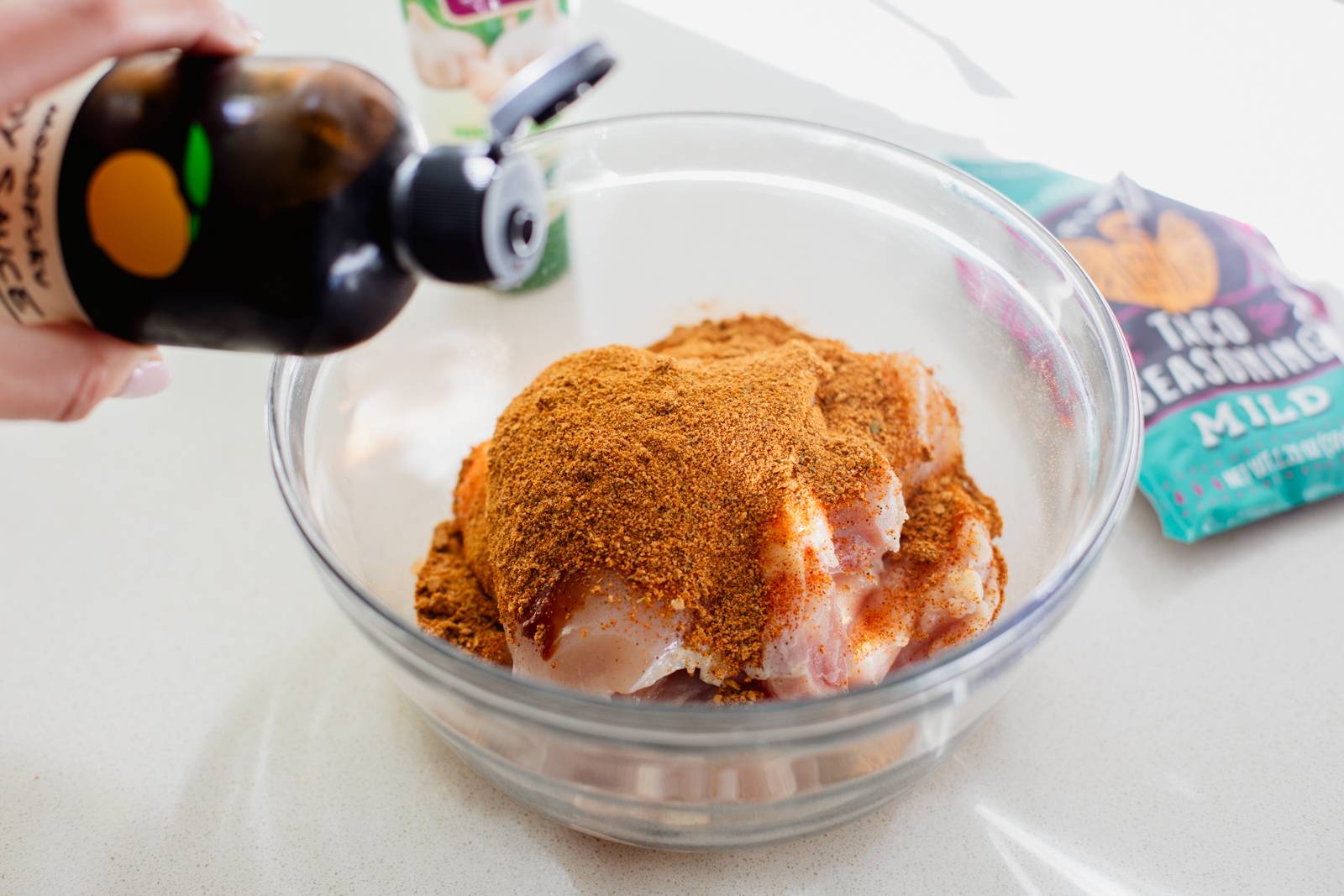 Sprinkling seasoning on raw chicken in a bowl.