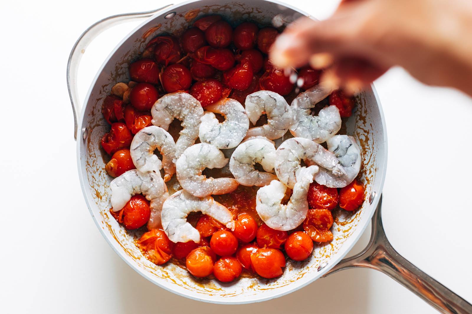 Raw shrimp being added to a pan with tomatoes