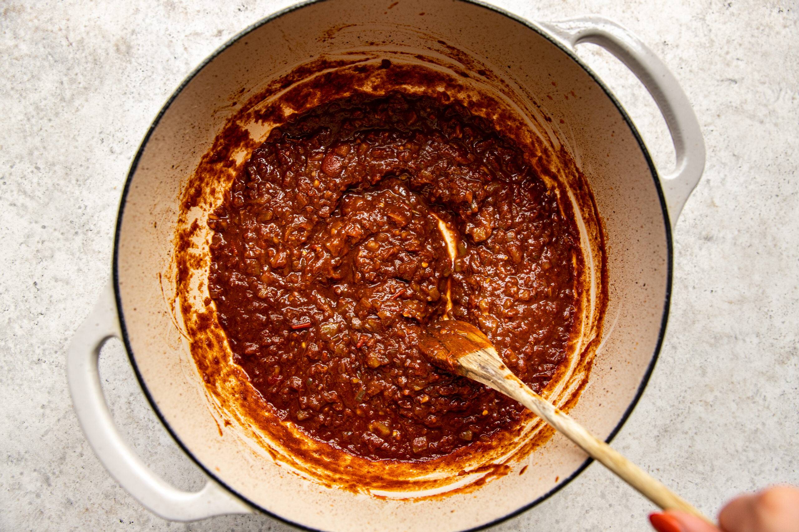 Cooking spices, tomatoes, and chilis in a dutch oven with onion and garlic.