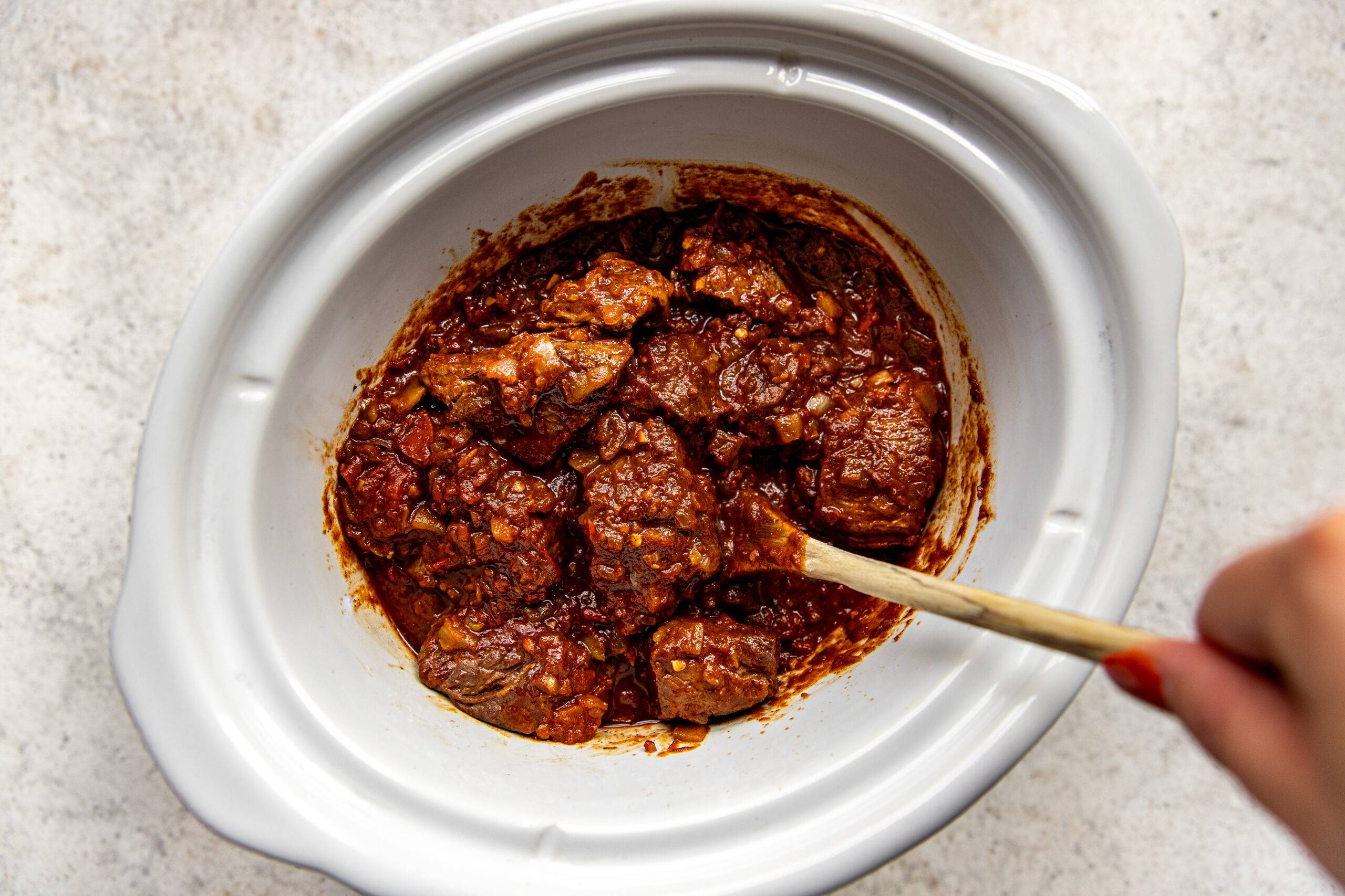 Stirring ingredients together with the beef in a slow cooker.