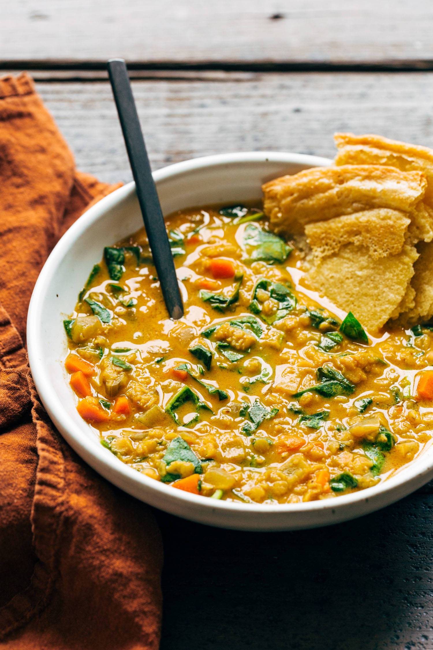 Red lentil soup with spinach and socca in a bowl with a spoon.