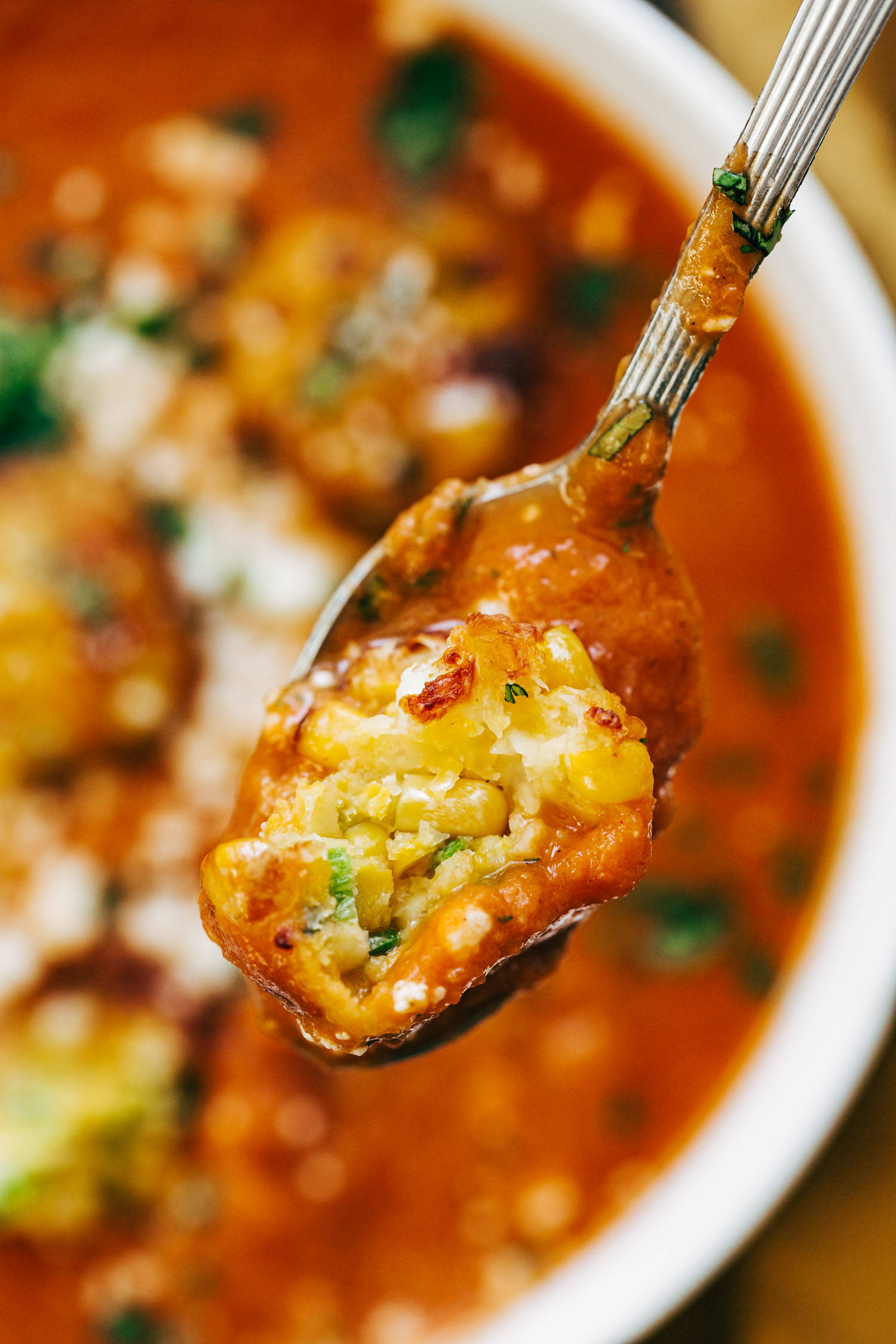 Spoon with a scoop of jalapeno corn fritters and sopa tarasca.