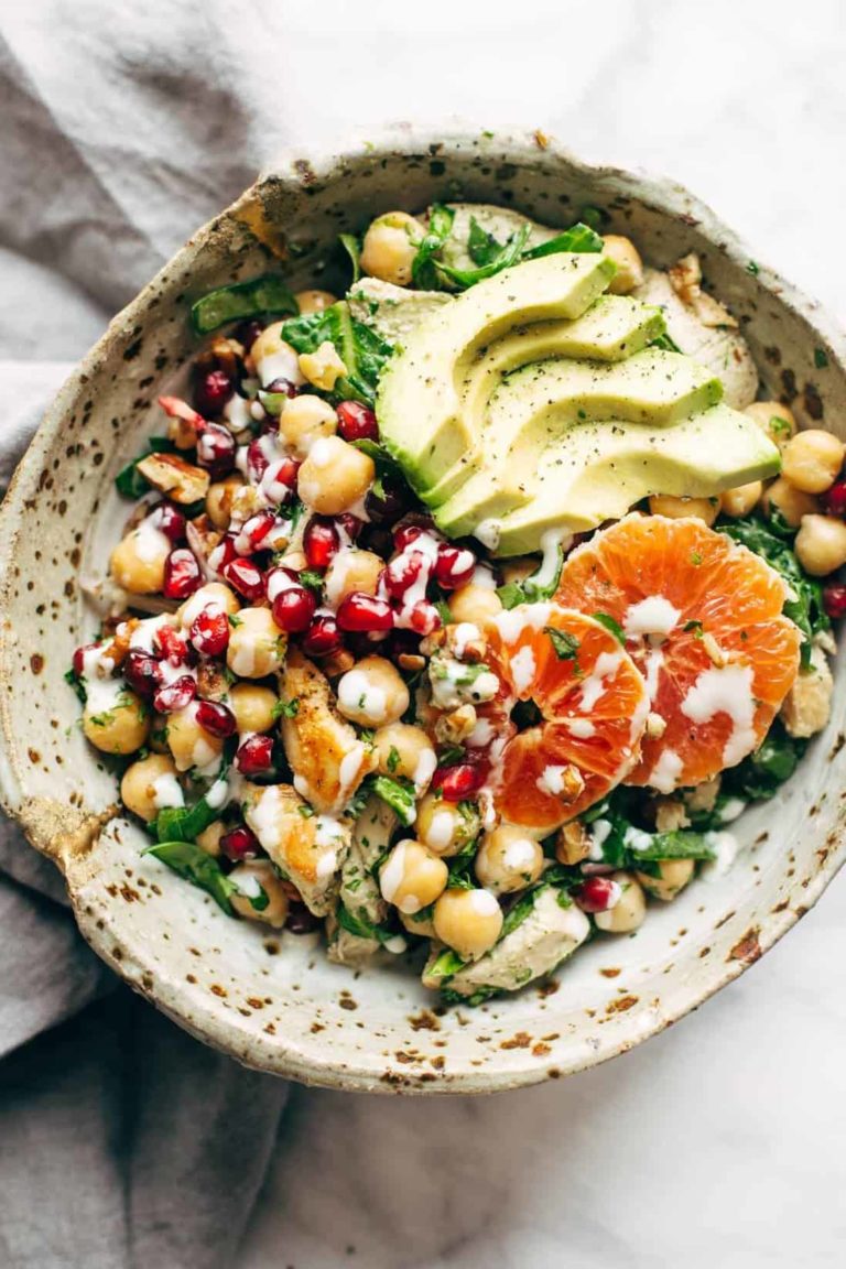 Spa salad in a bowl topped with chicken, avocado, and oranges.