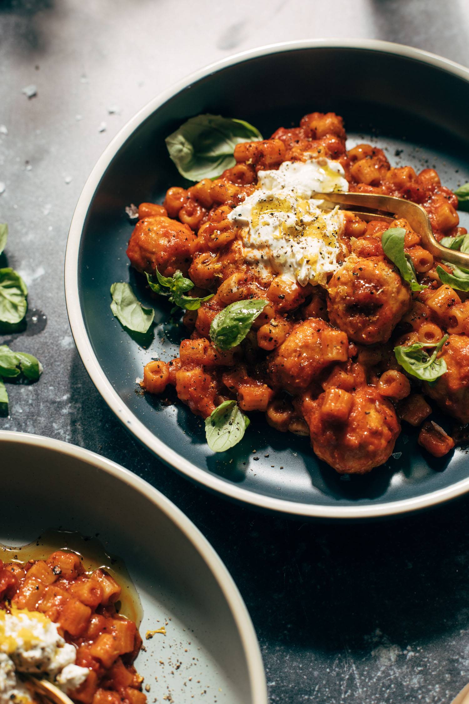 Pasta and meatballs with ricotta on a plate, sprinkled with fresh basil.