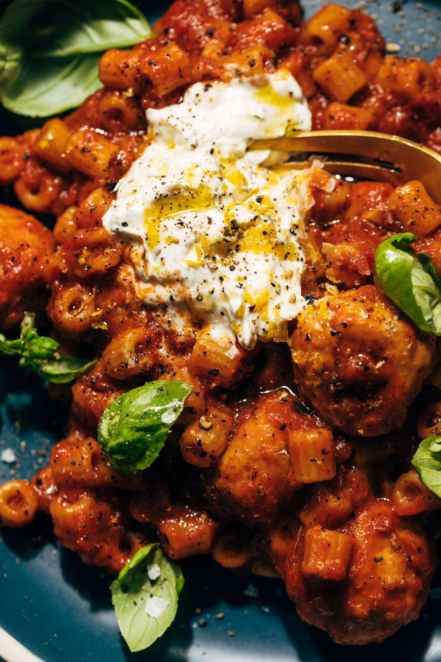 Fork scooping up pasta and meatballs with ricotta.