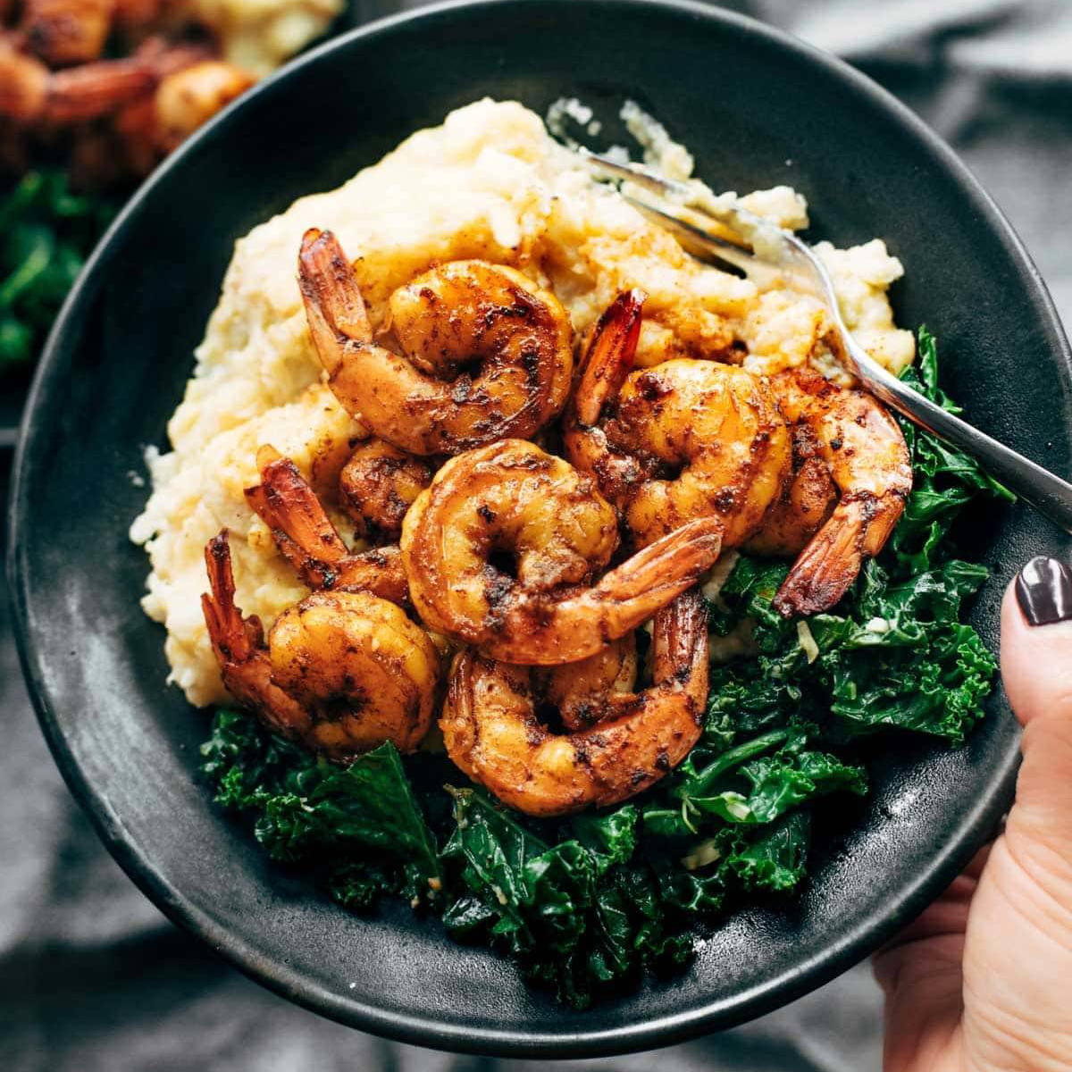 Spicy shrimp in a bowl with cauliflower mash and sautéed kale.