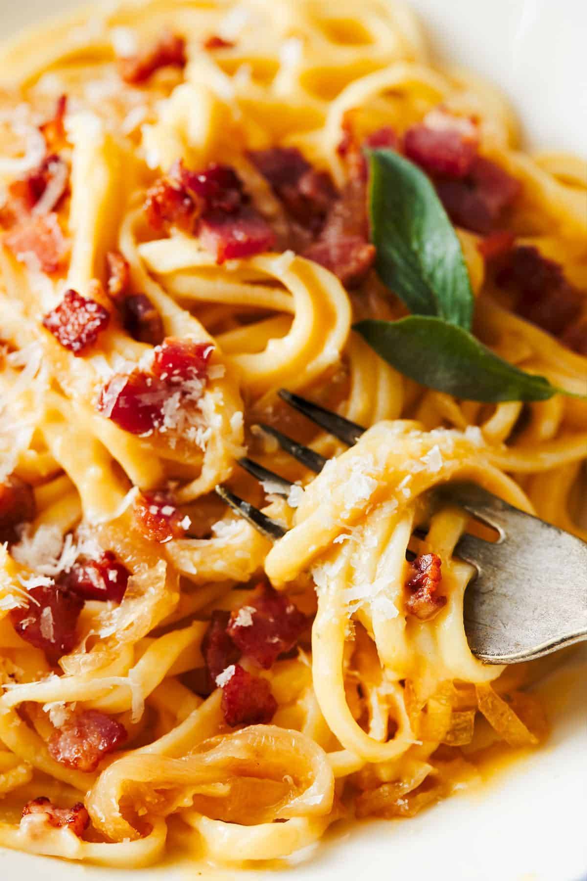 Fettuccini with caramelized onions dotted with pieces of pancetta in a bowl with a fork.