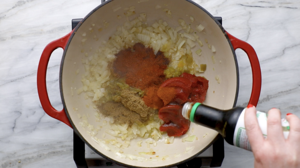 Adding spices and canned ingredients to chili.