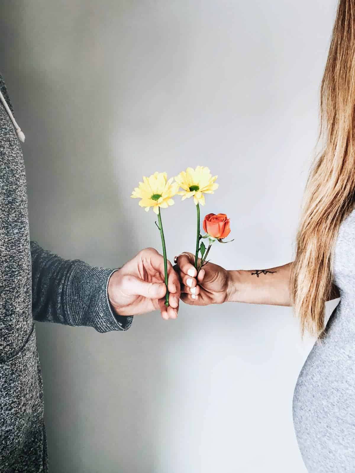 One man and a woman is holding flowers in their hands and holding hands together.