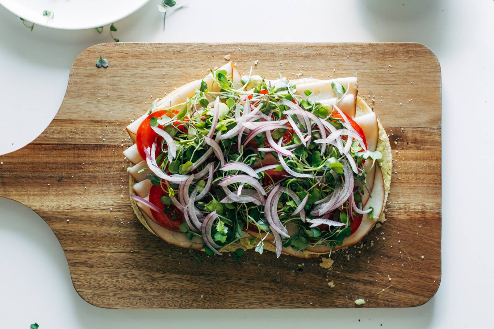 Turkey, tomato, greens, and red onion being added to a piece of focaccia bread