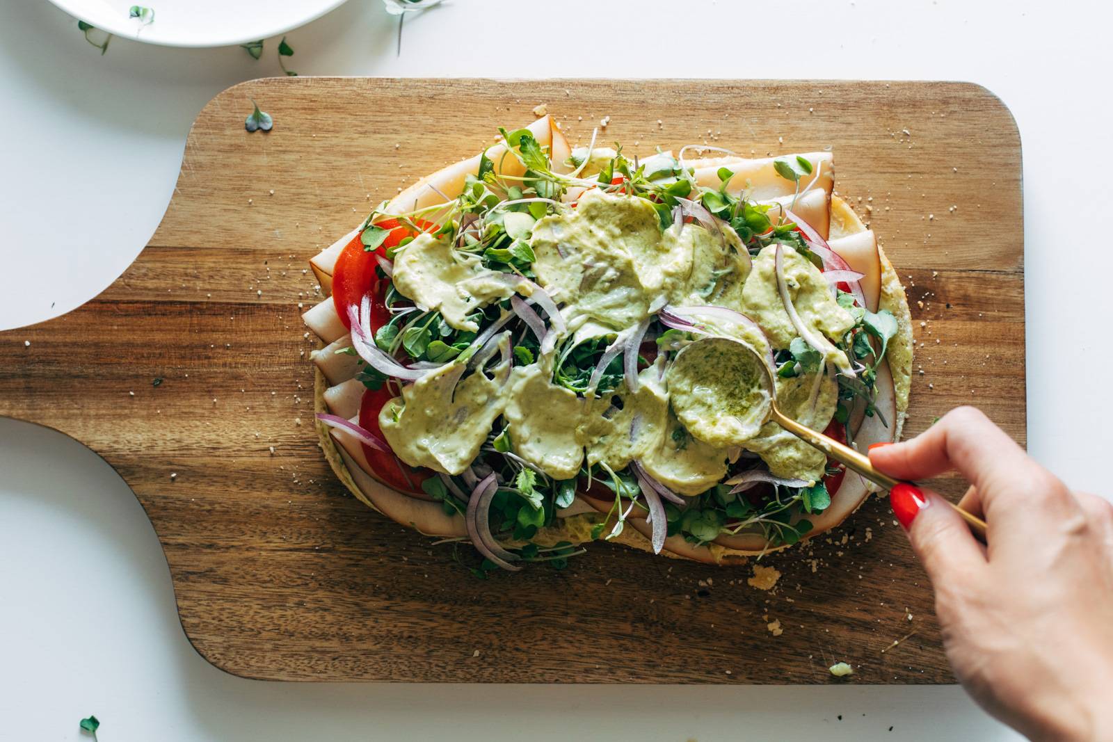 Pesto mayo being added to the top of a turkey sandwich on focaccia bread