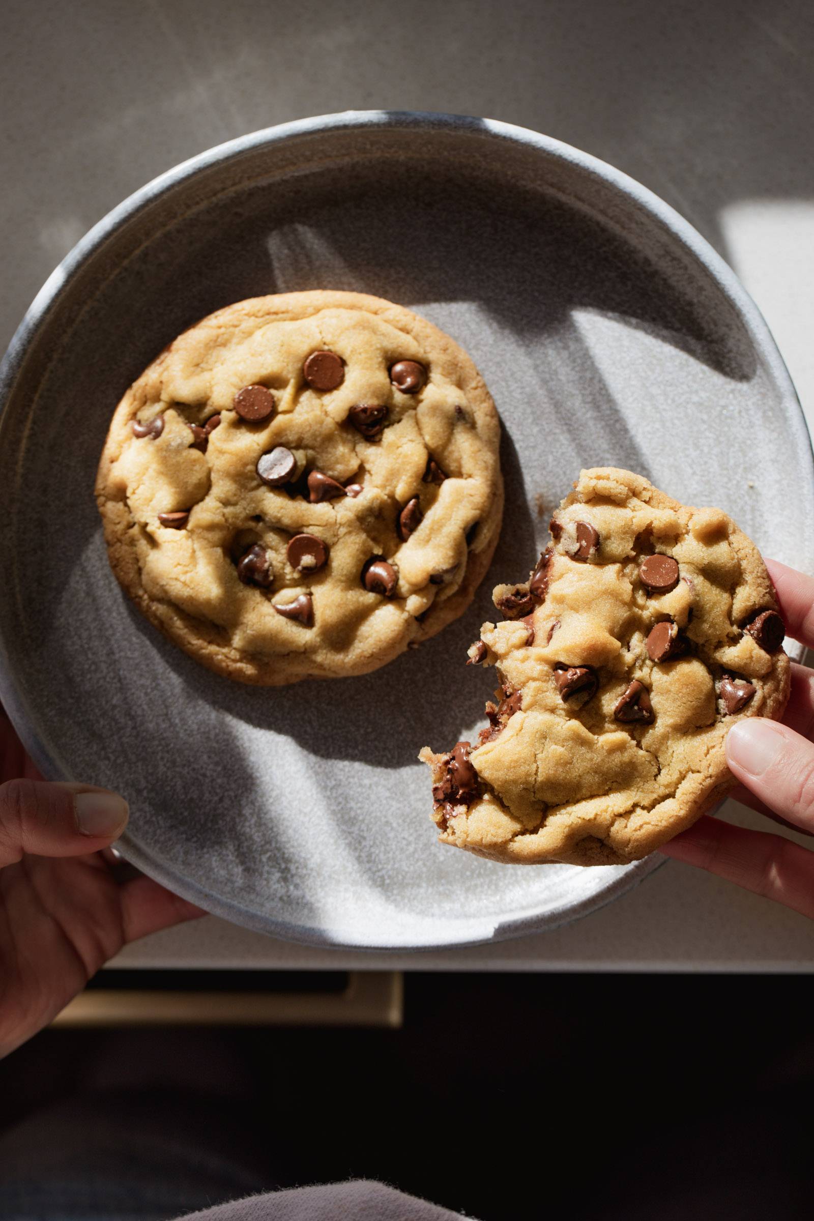 Hand holding a half-eaten chocolate chip cookie.