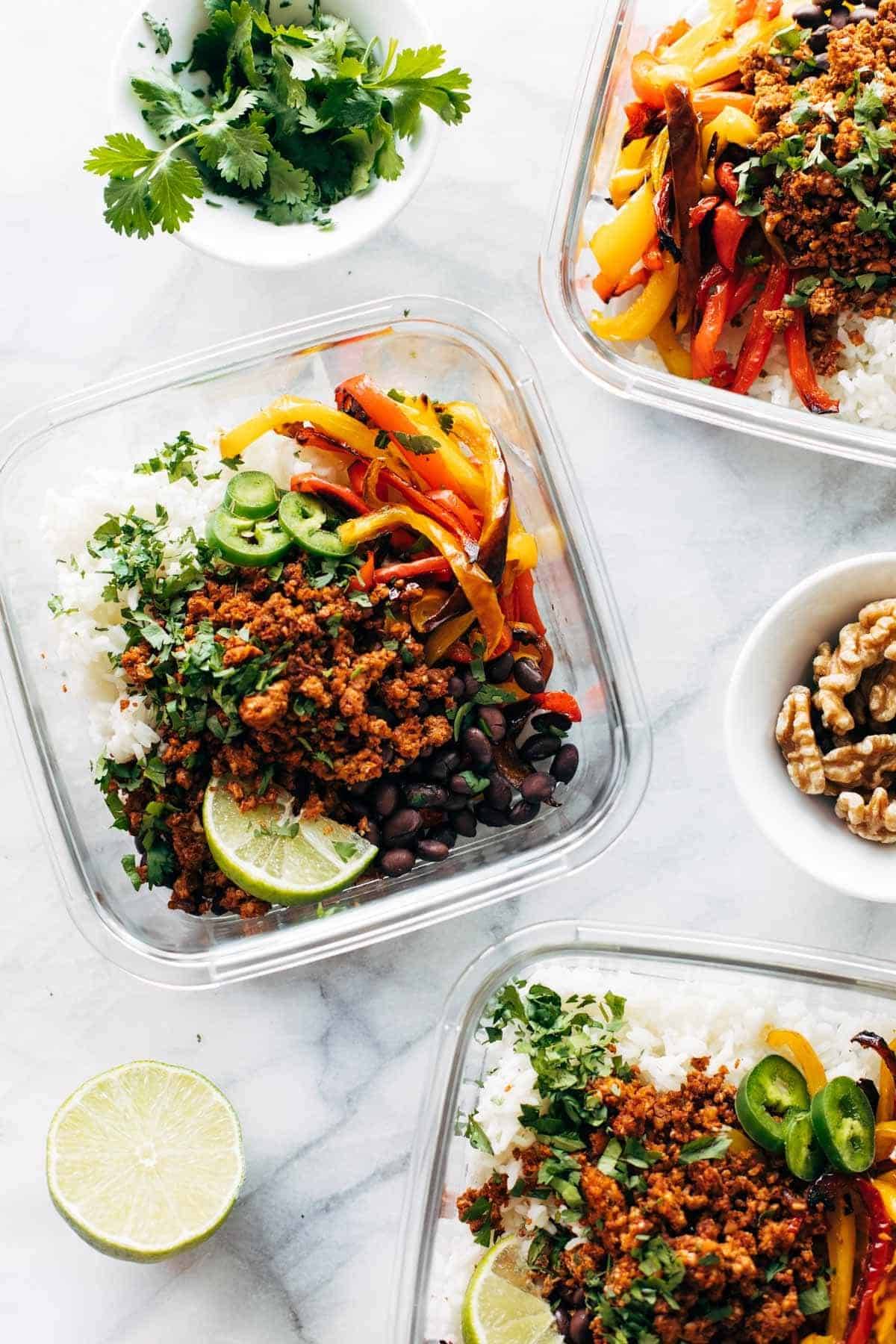 Jalapeno peppers, vegan taco meat, black beans, lime wedges, and red and orange bell peppers in a clear bowl over rice.