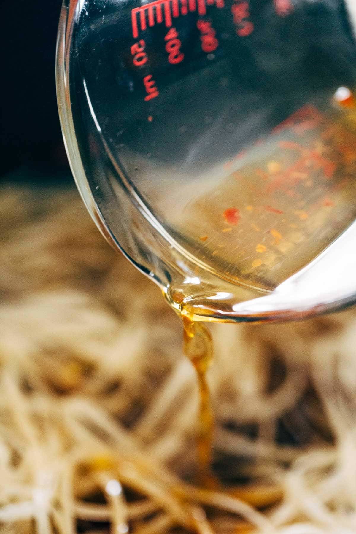 Measuring cup pouring sauce on to pad thai noodles