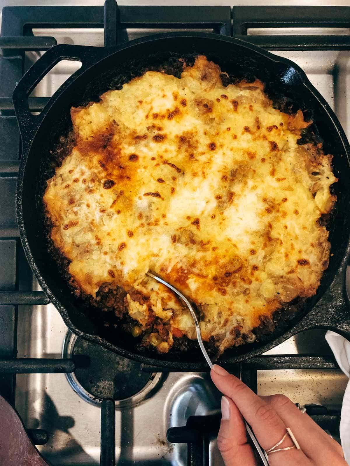 A person holds a utensil in a black pan of food.